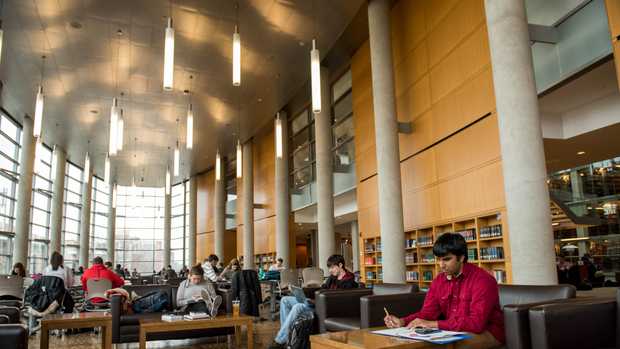 large library study room with variety of young adults studying at tables or on soft chair